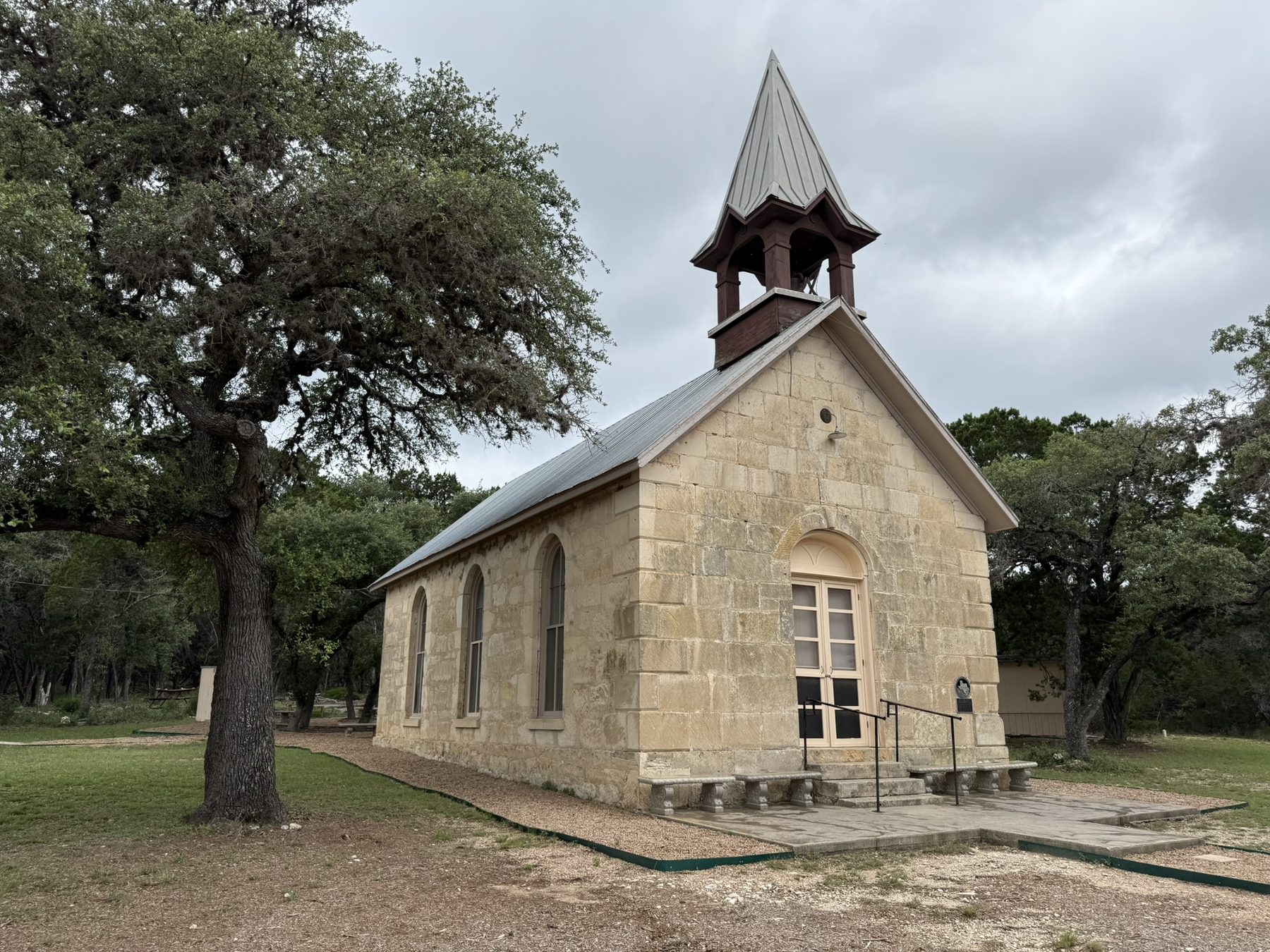 The limestone facade of Polly's Chapel with its bell tower, framed by oak trees