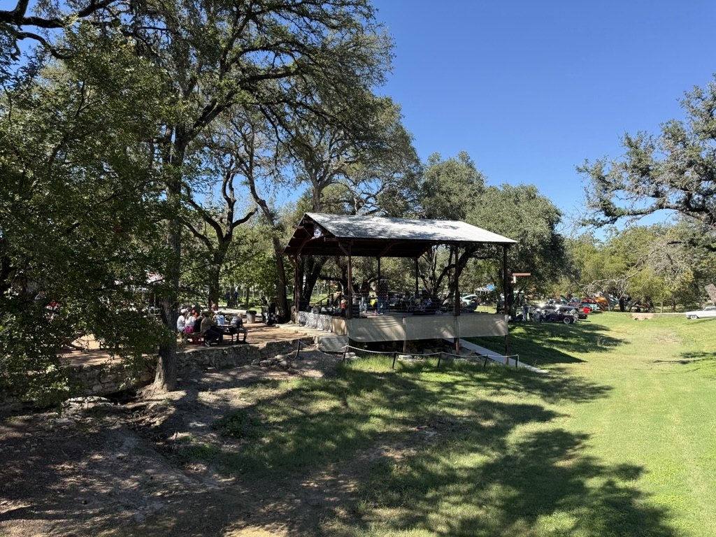 The pavilion under the oaks on a clear afternoon, picnic tables and a car show alongside