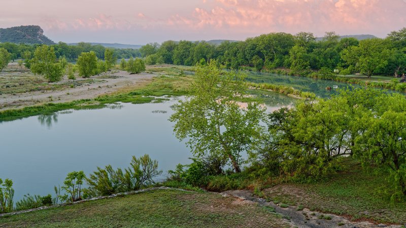 The South Llano River at dawn in Junction, with trees along the bank and a limestone bluff in the distance